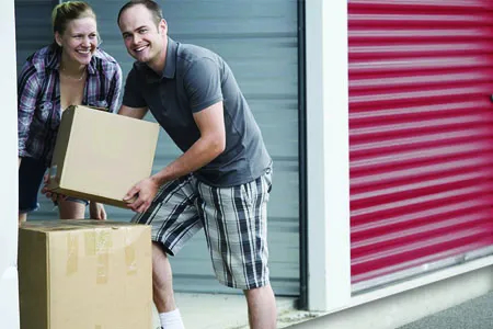 A couple moving several cardboard boxes into a storage unit.