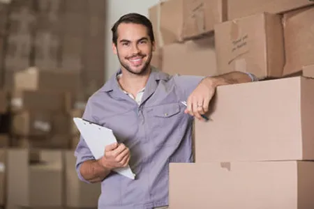 A man posing with a clipboard and a large stack of boxes.