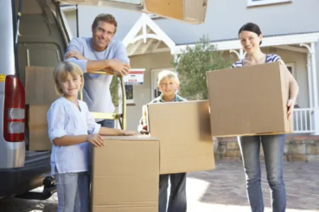 A family of four standing in front of a car with moving boxes.